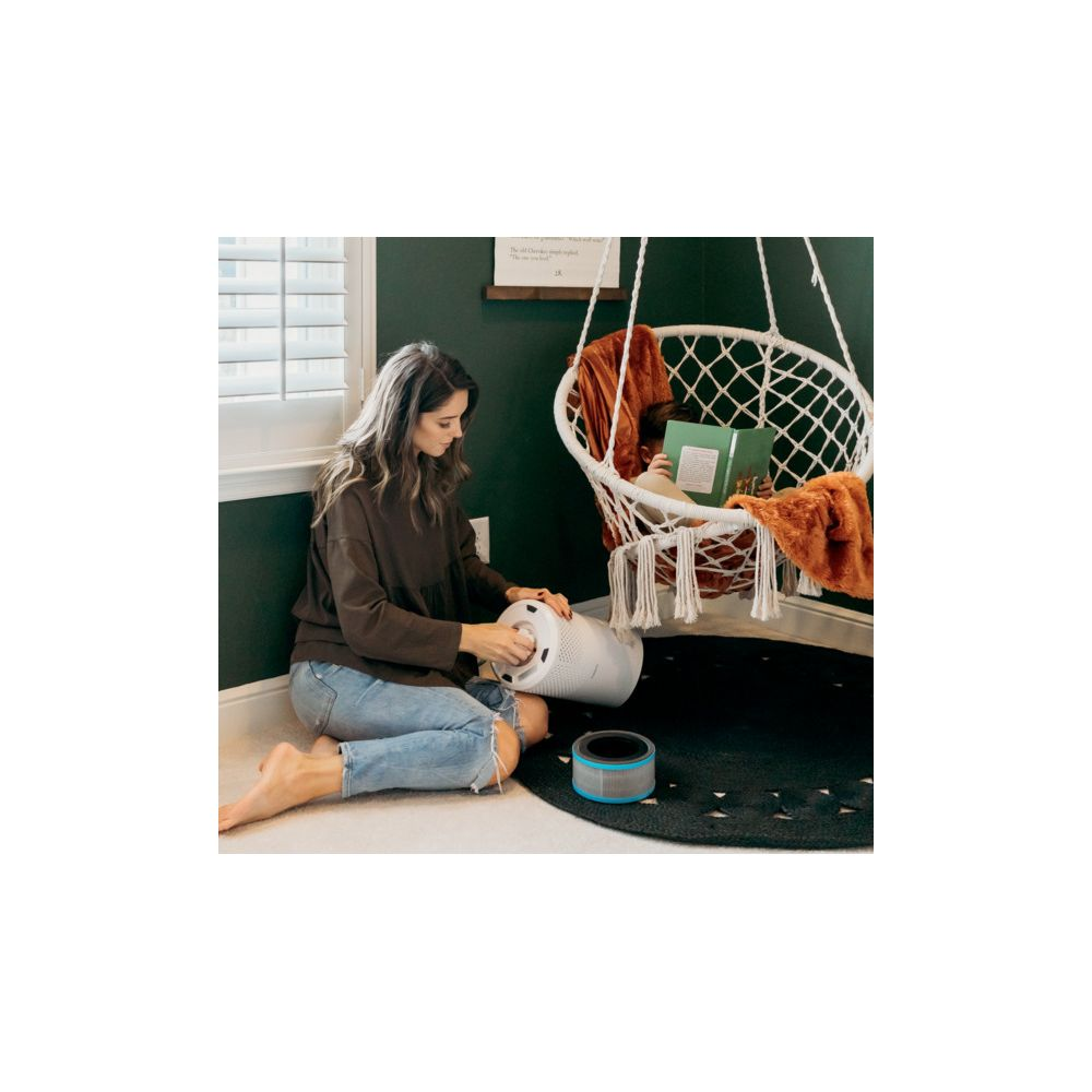 Kobieta siedzi na podłodze, zmieniając filtr powietrza w białej oczyszczarce.