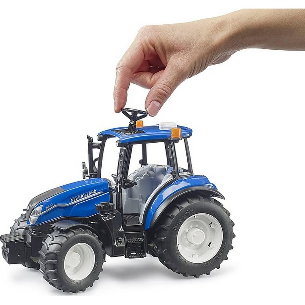 Eine Hand dreht das Lenkrad eines blauen Spielzeugtraktors auf weißem Grund.
