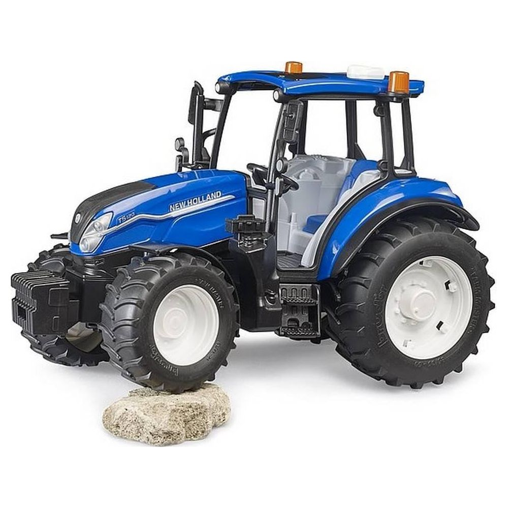 Ein blauer New Holland Traktor mit großen Rädern steht auf einem Stein.