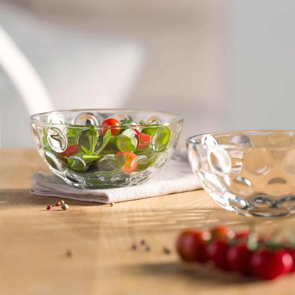 Zwei Glasschalen auf einem Holztisch, eine gefüllt mit Salat, die andere leer.