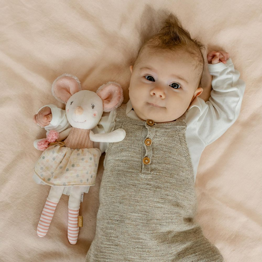Un bambino giace accanto a un topolino di peluche su un lenzuolo rosa.