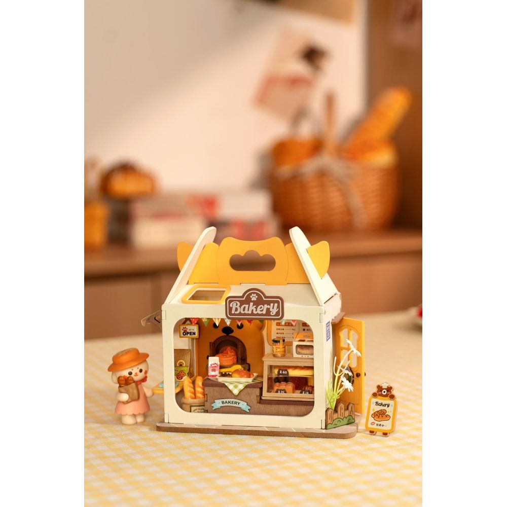 Panificio in miniatura con figura, forno, espositori e cesti sullo sfondo.