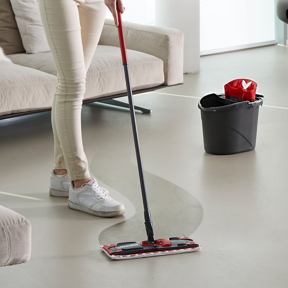 Eine Person wischt den Boden mit einem roten und grauen Wischmopp in einem modernen Wohnzimmer.