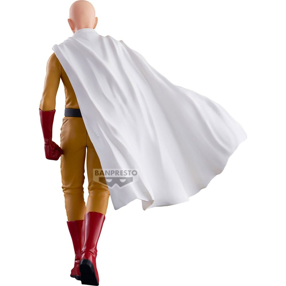 Una figura calva con traje amarillo, guantes y botas rojas, lleva una capa blanca ondeante.
