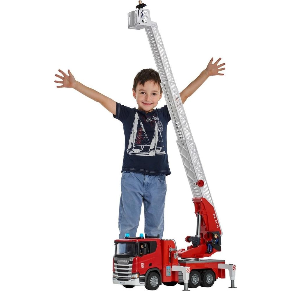Chłopiec stoi na czerwonej drabinie wozu strażackiego z wysuniętym koszem. Białe tło.