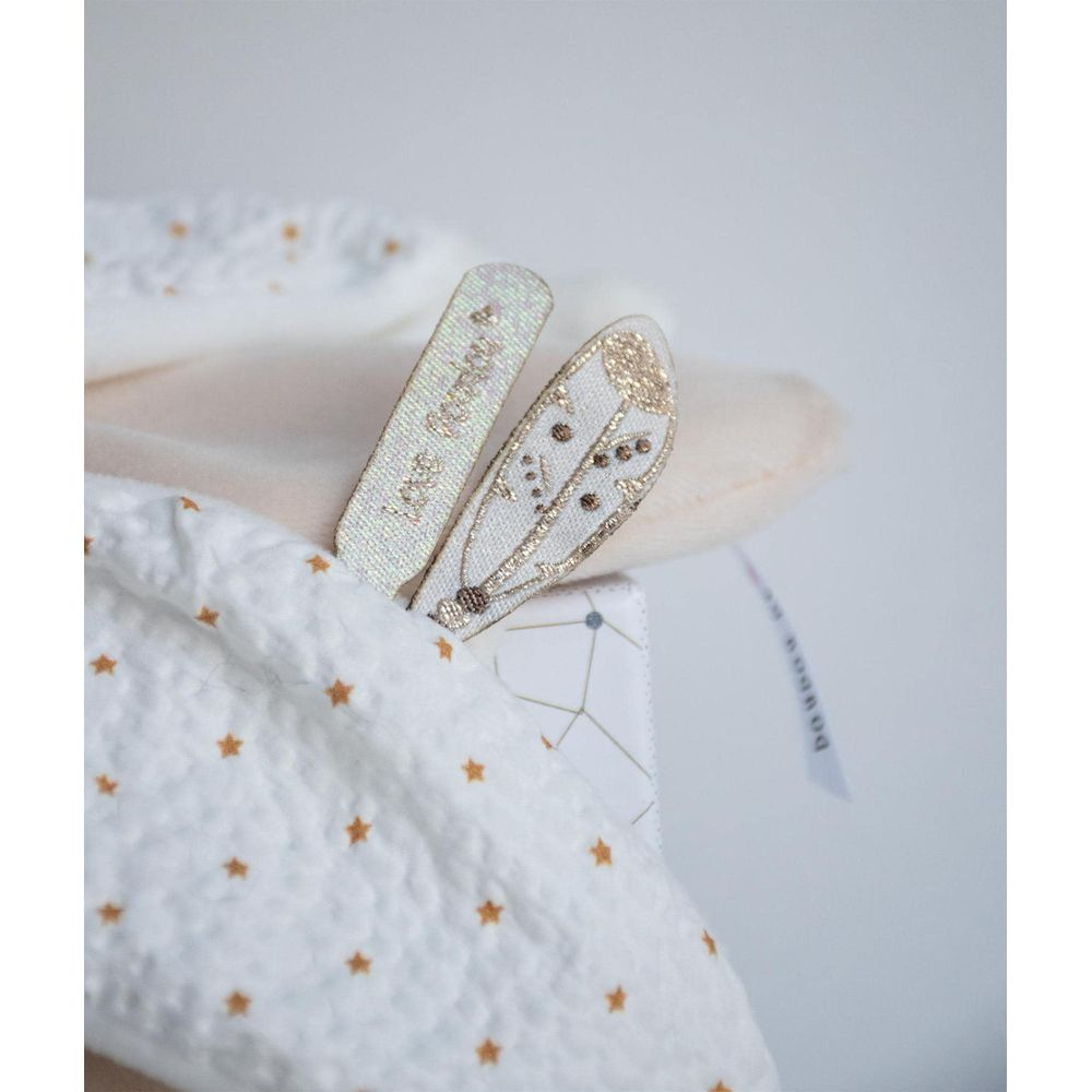 Biała pluszowa zabawka z motywem gwiazd i złotymi uszami z piórkiem.