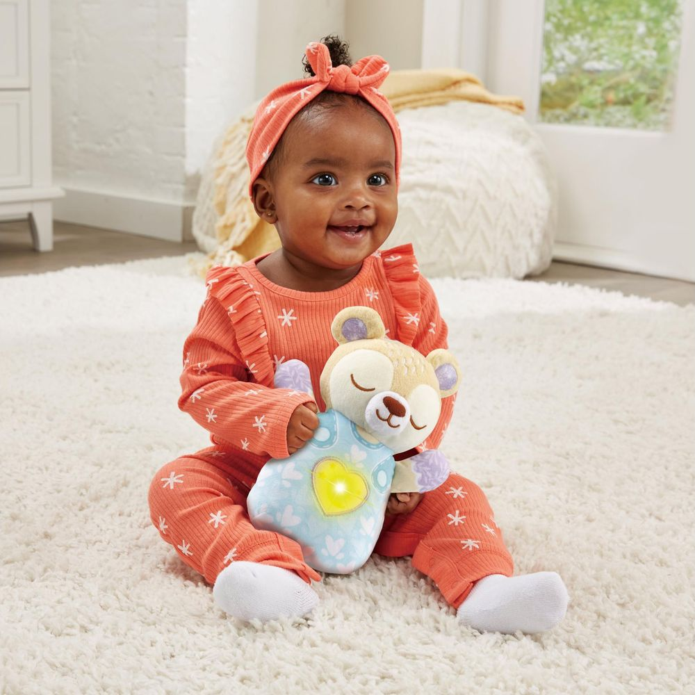 Ein Baby in einem orangefarbenen Outfit hält einen leuchtenden Teddybär.