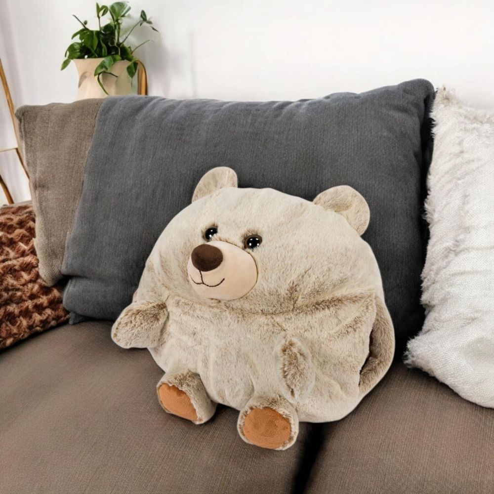 Ein flauschiges, beiges Teddybär-Kissen sitzt auf einer Couch mit Kissen dahinter.