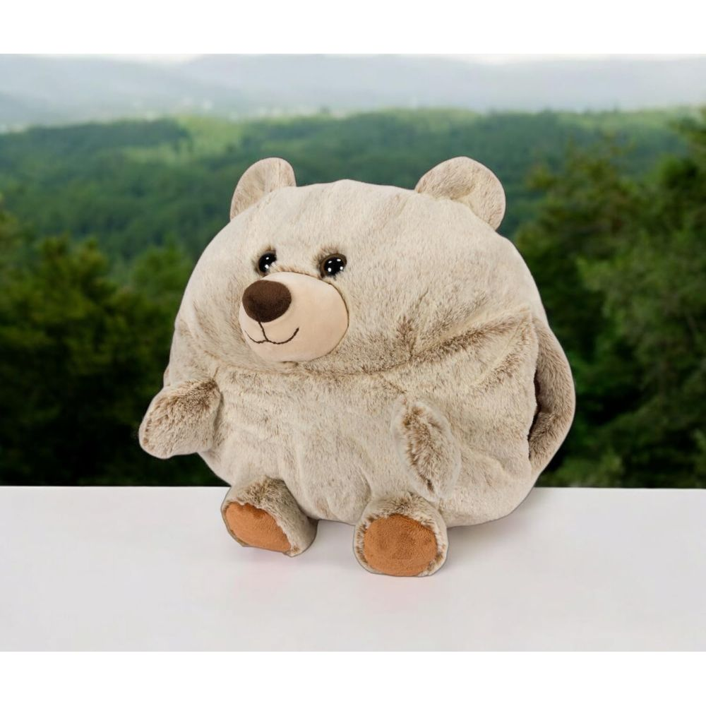 Ein runder, beiger Teddybär sitzt auf einem weißen Tisch vor einem Wald.