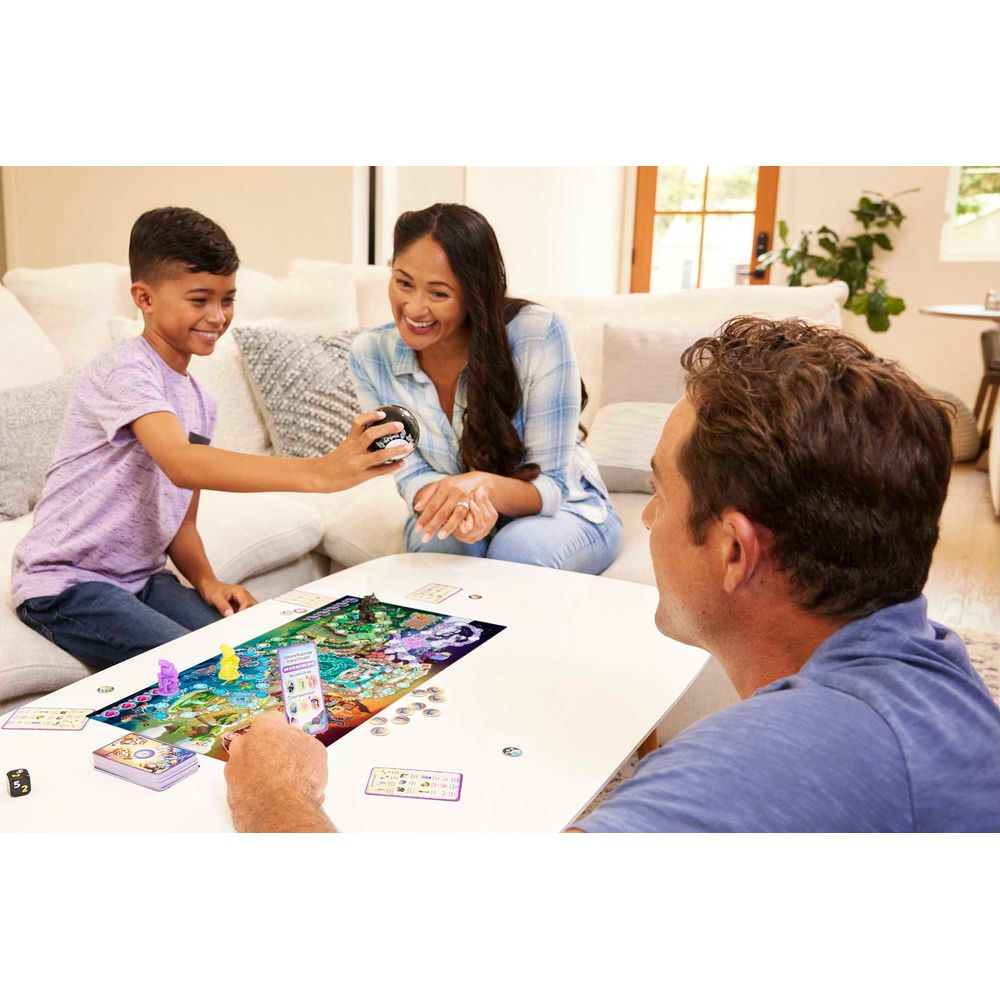Eine Familie spielt ein Brettspiel im Wohnzimmer. Der Junge hält einen Ball.