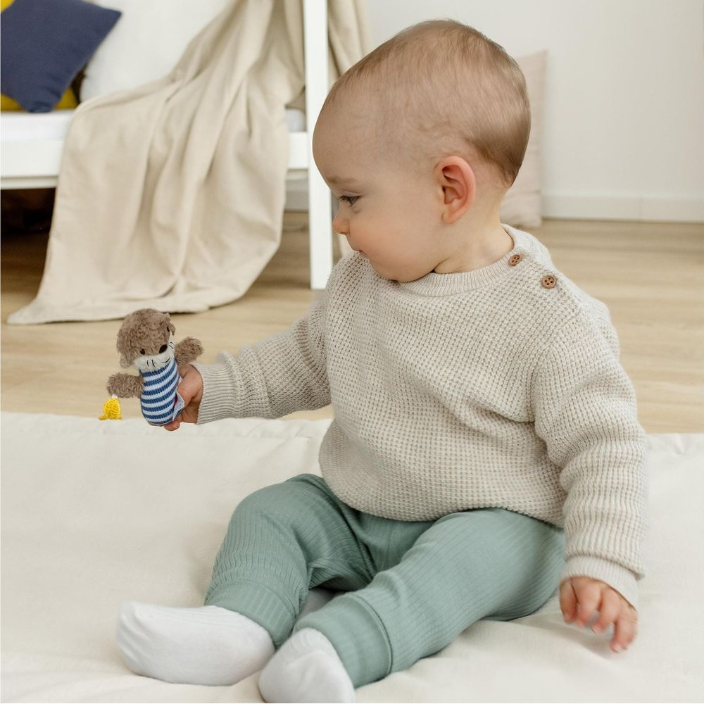 Un bambino è seduto su una coperta bianca, tiene in mano un piccolo peluche.