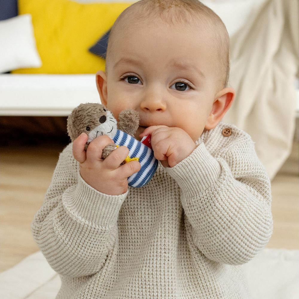 Bambino in maglione beige tiene un giocattolo di lontra imbottito a strisce blu e bianche alla bocca.
