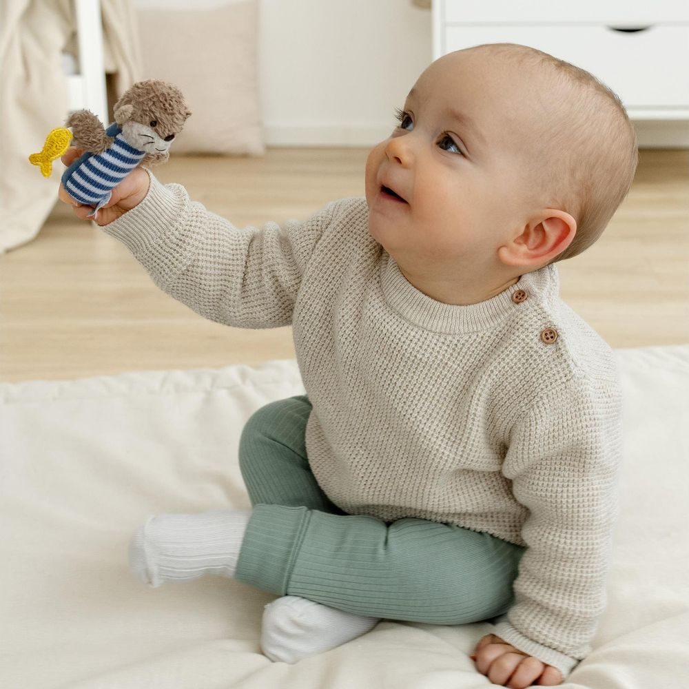 Bambino in maglione beige e pantaloni verdi tiene un peluche con pesce.