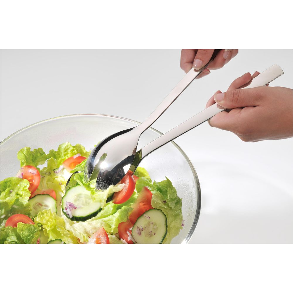 Hände servieren Salat mit Besteck aus einer Glasschüssel mit Tomaten und Gurken.