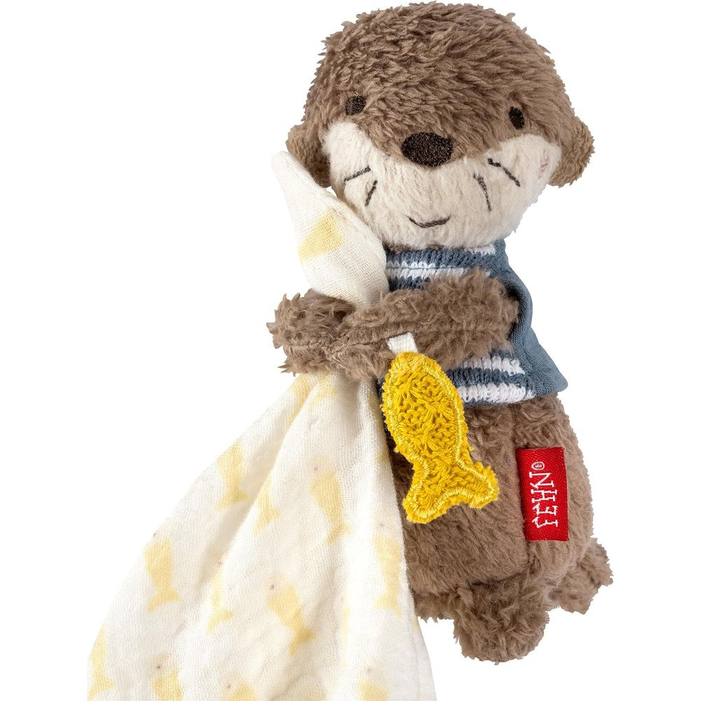 Peluche lontra marrone con maglione a righe blu e bianche tiene un'applique a forma di pesce giallo e un telo.