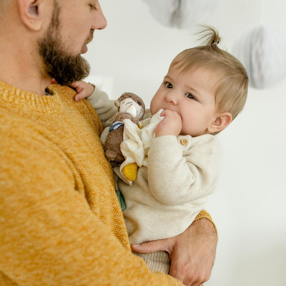 Un uomo barbuto in maglione giallo senape tiene un bambino. Il bambino tiene un peluche.