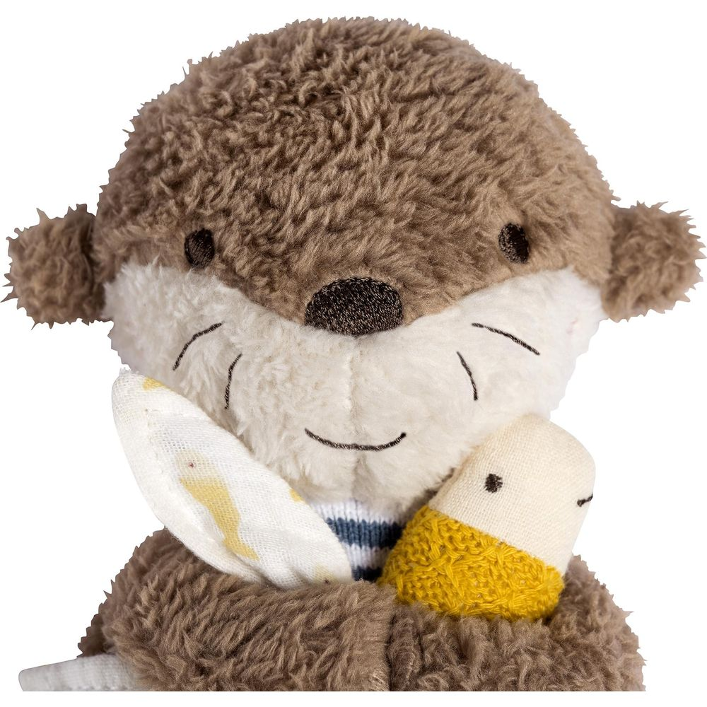 Ein Stoffotter mit braunem Fell, das ein weißes Tuch und eine gelbe Karotte hält.