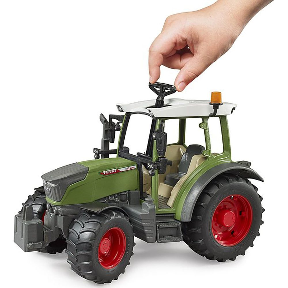 Ein grüner Spielzeugtraktor mit roter Felge. Eine Hand dreht das Lenkrad.