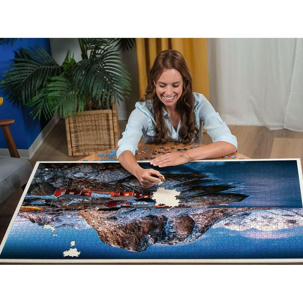 Frau puzzelt ein Bild von roten Häusern an einem felsigen Ufer mit Spiegelung.