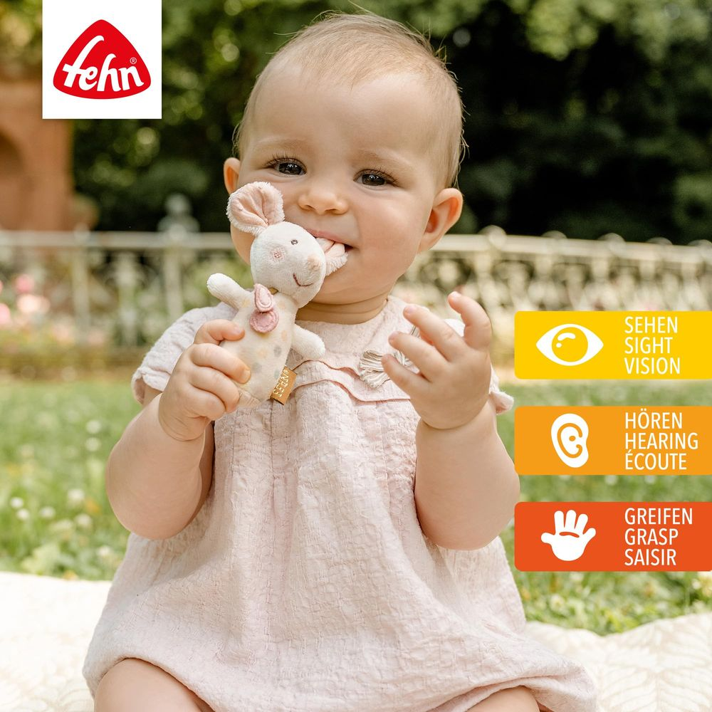 Bébé en robe rose mordillant un doudou lapin avec logo Fehn.
