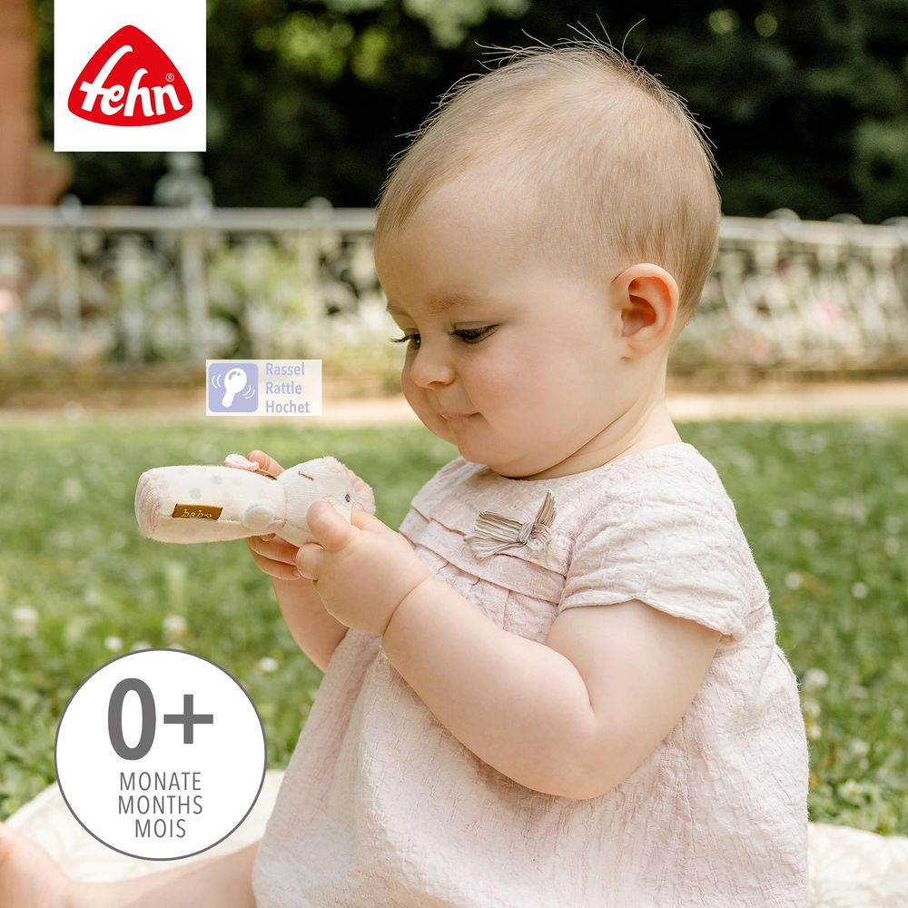 Bébé en robe rose joue avec un hochet clair à l'extérieur.