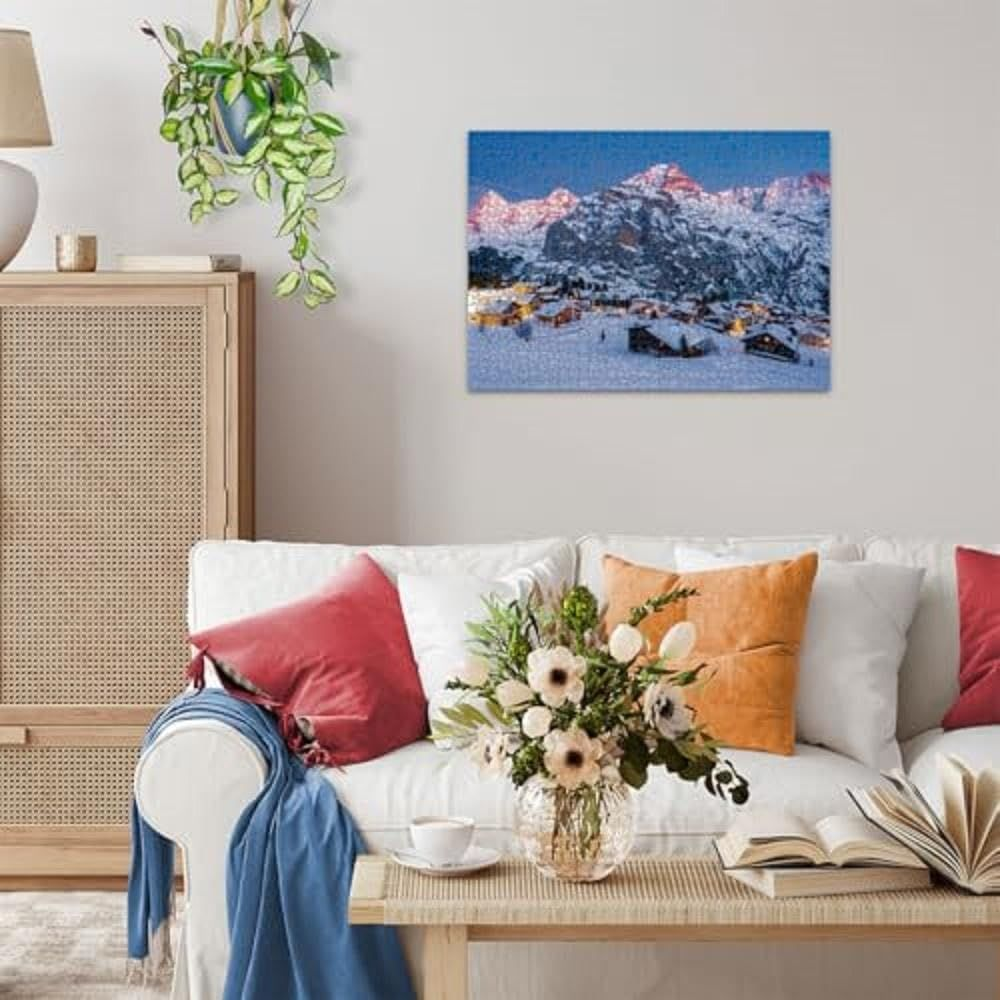 Schneebedeckte Berge über einem verschneiten Dorf bei Nacht mit beleuchteten Fenstern.