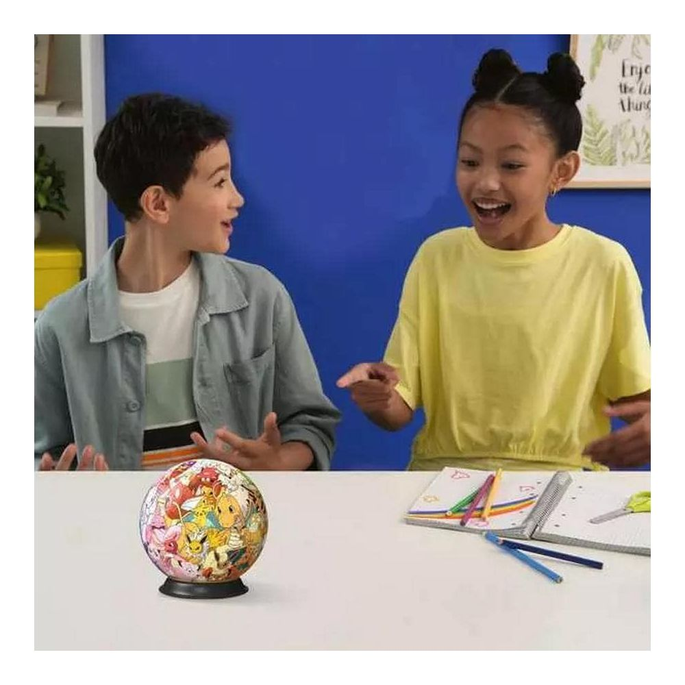 Dwoje dzieci siedzi przy stole z globusem Pokémon i artykułami piśmienniczymi.