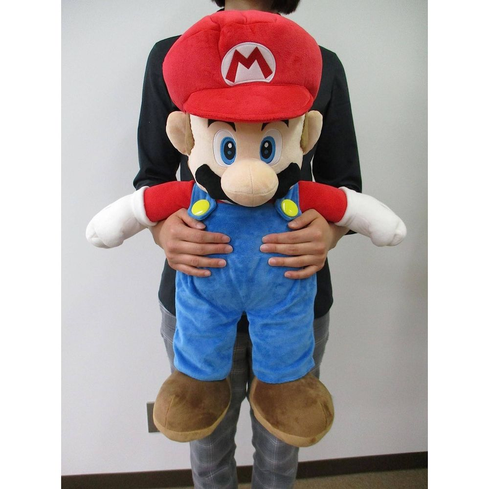 Una persona tiene un grande peluche di Mario con cappello rosso e salopette blu.