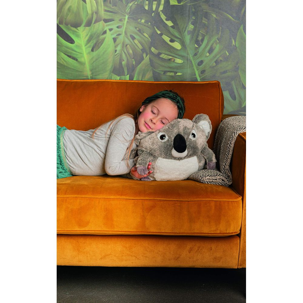 Mädchen schläft auf orangefarbenem Sofa mit Koala-Kissen, Hintergrund mit Blättern.