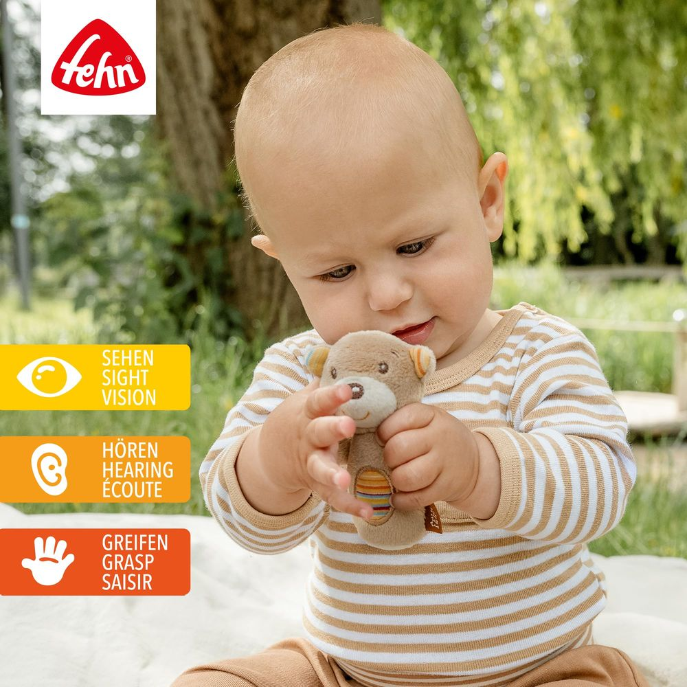 Baby hält einen Teddybär, mit Hinweis-Symbolen für Sehen, Hören, Greifen.