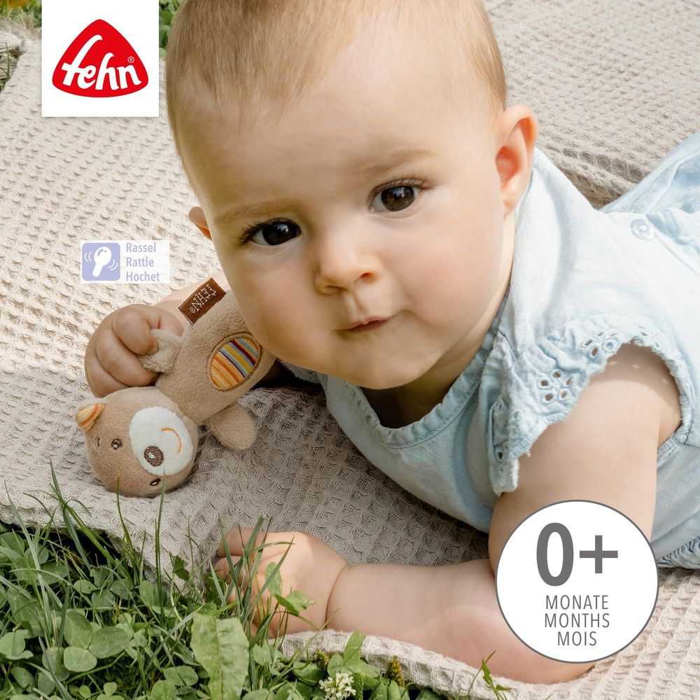Ein Baby liegt auf einer Decke und hält einen Teddybären. Fehn-Logo oben links.