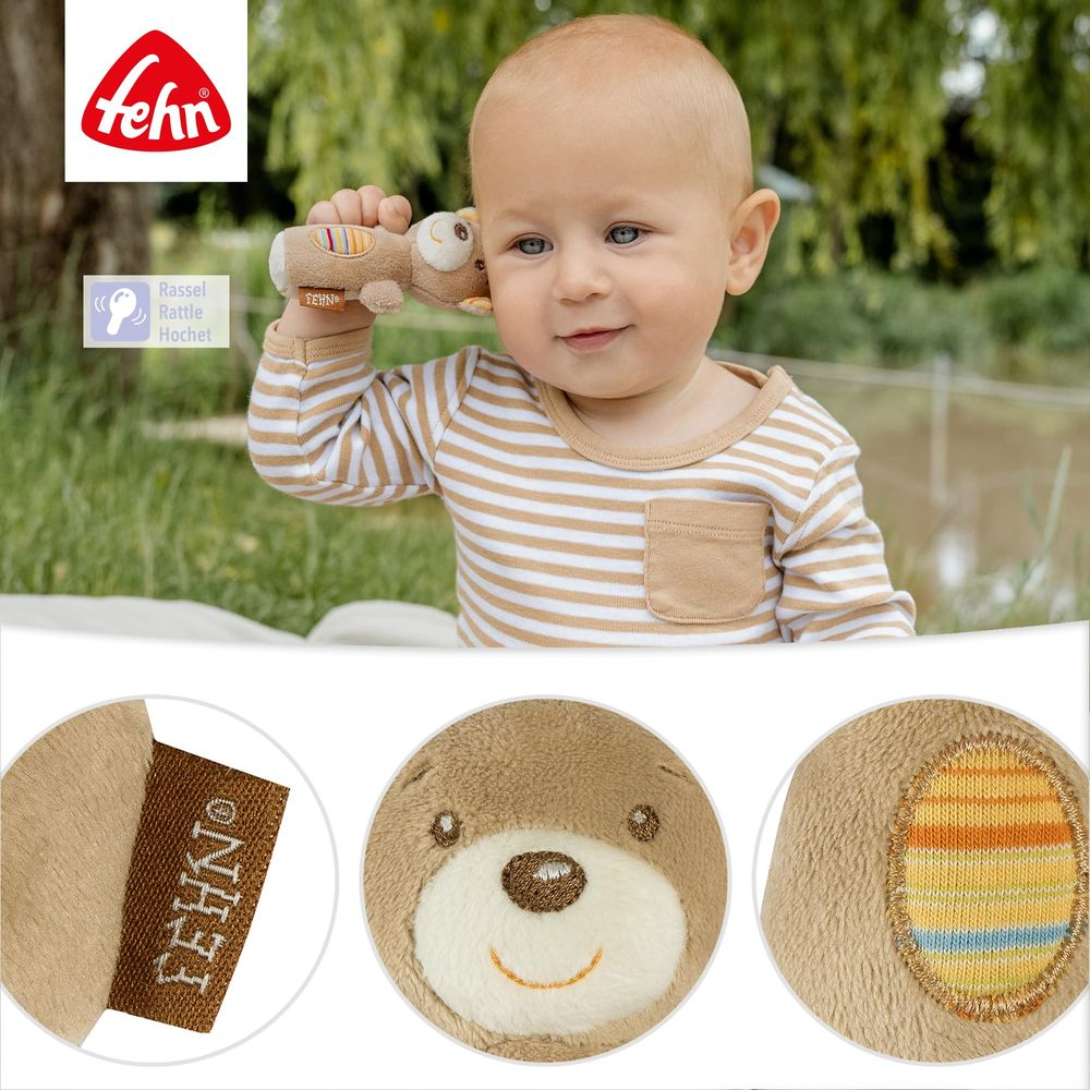 Baby in gestreiftem Shirt hält eine Plüschbär-Rassel ans Ohr. Nahaufnahmen zeigen Etikett und Bärenkopf.