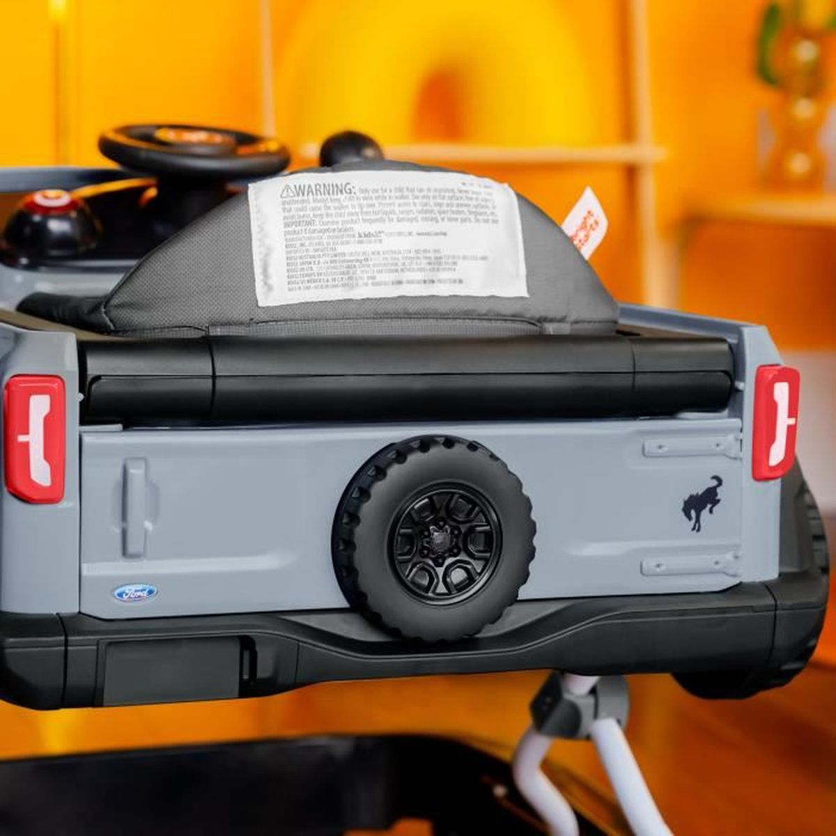 Graues Spielzeugauto mit Ersatzrad und rotem Rücklicht. Warnhinweis auf der Rückseite.