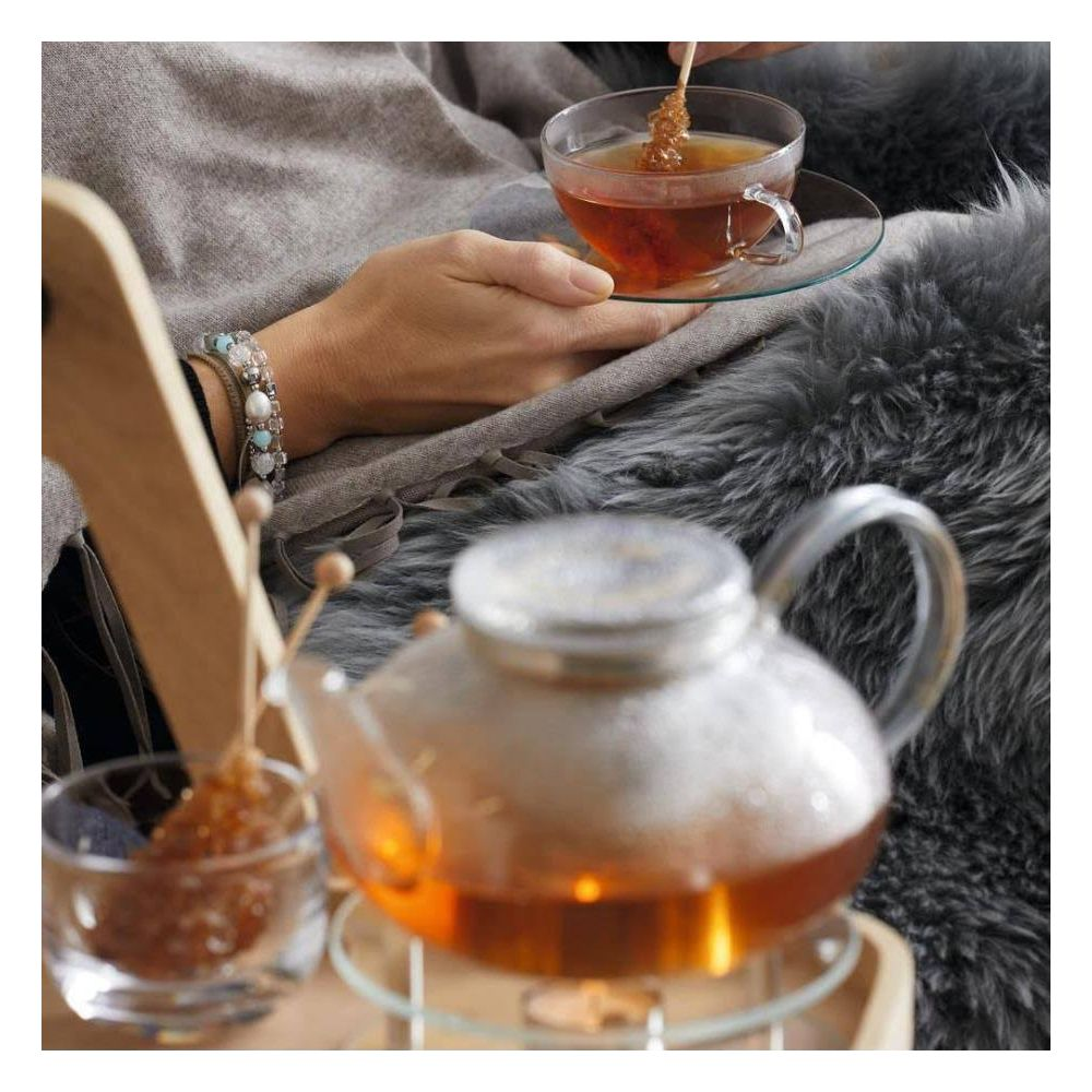 Hände halten eine Teetasse mit Kandiszucker und eine Teekanne aus Glas.