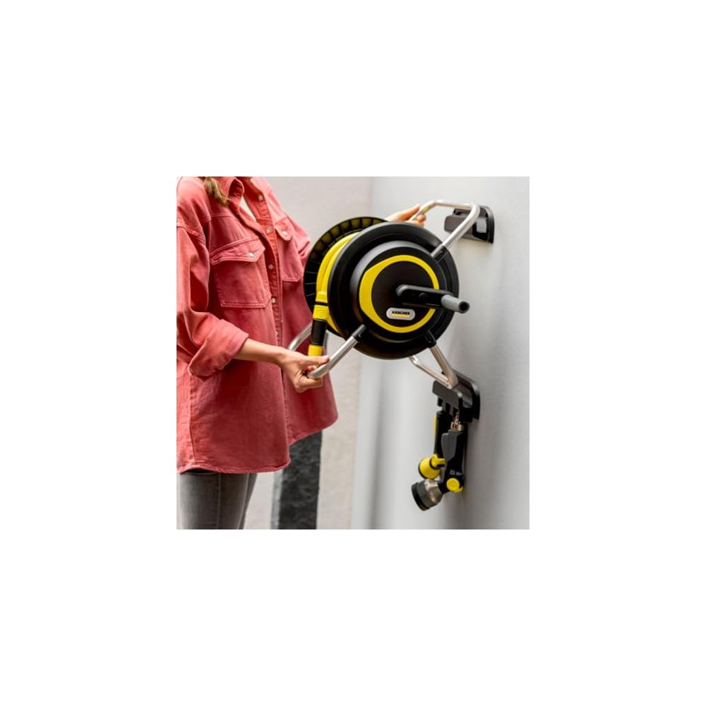 Una persona monta un enrollador de manguera negro y amarillo en una pared.