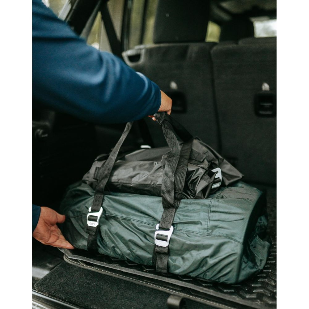 Persona che carica borse da viaggio verde scuro e nere nel bagagliaio di un'auto.