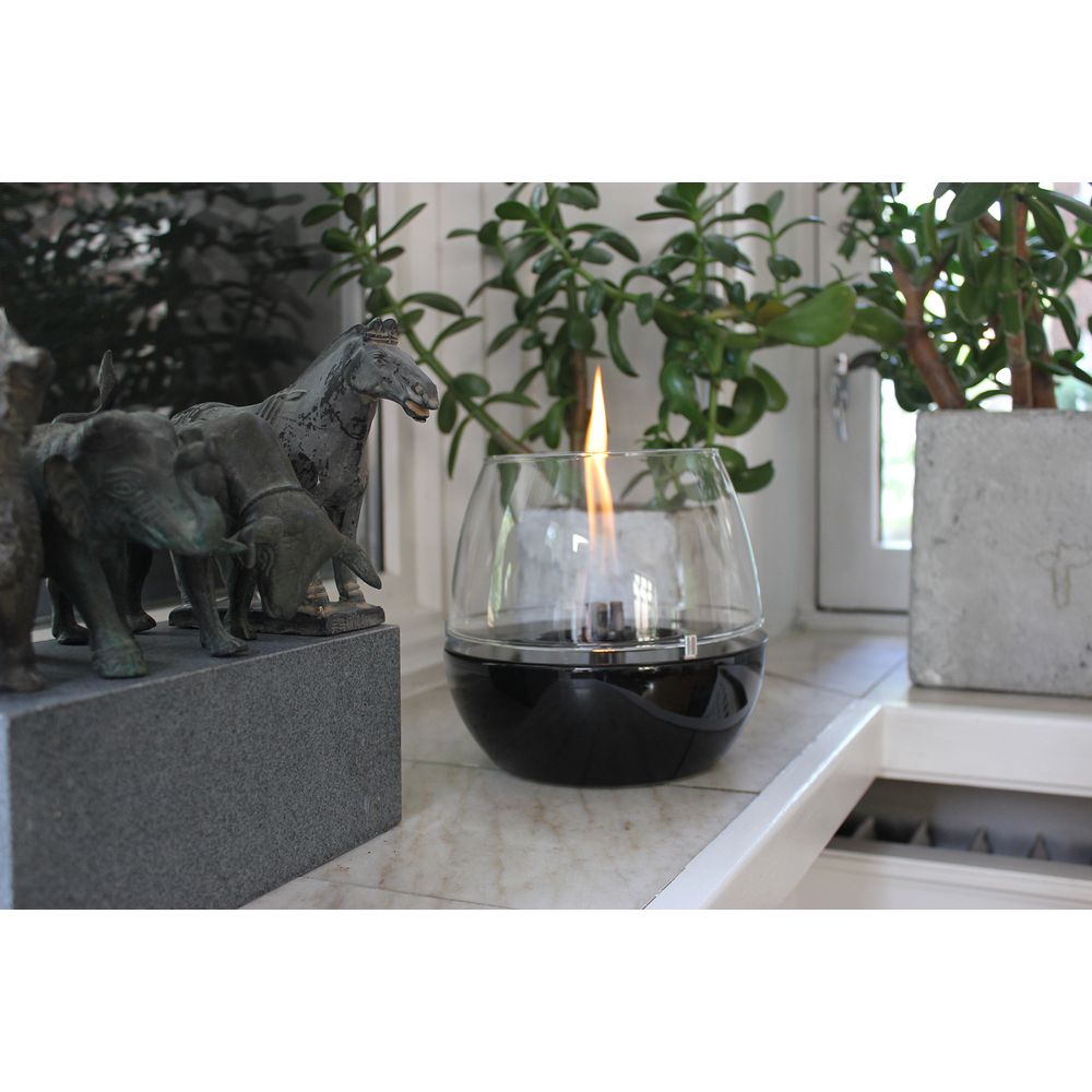 Lampada a olio in vetro con fiamma su marmo vicino a statue di animali e piante.