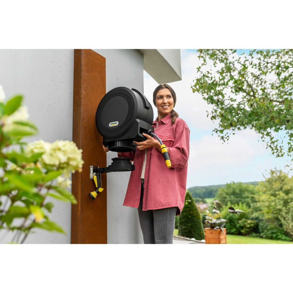 Frau hält Schlauchaufroller mit Schlauch in einem Garten.