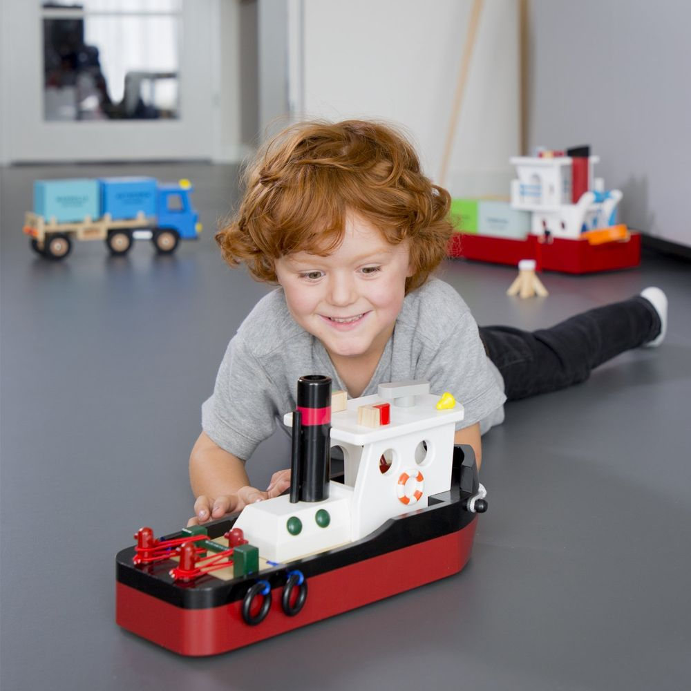 Ein rothaariger Junge spielt auf dem Boden mit einem Spielzeugboot.