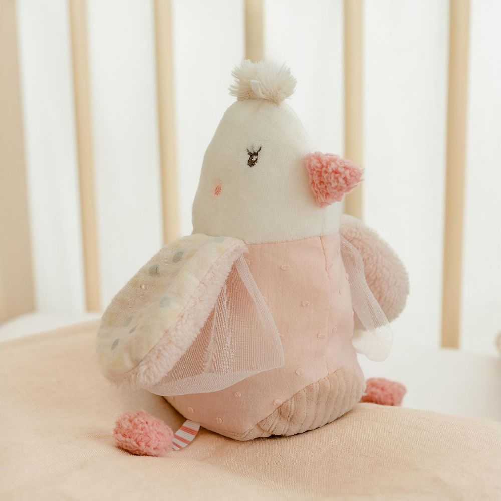 Un uccello giocattolo di peluche rosa e bianco con ali a pois siede su una coperta rosa.