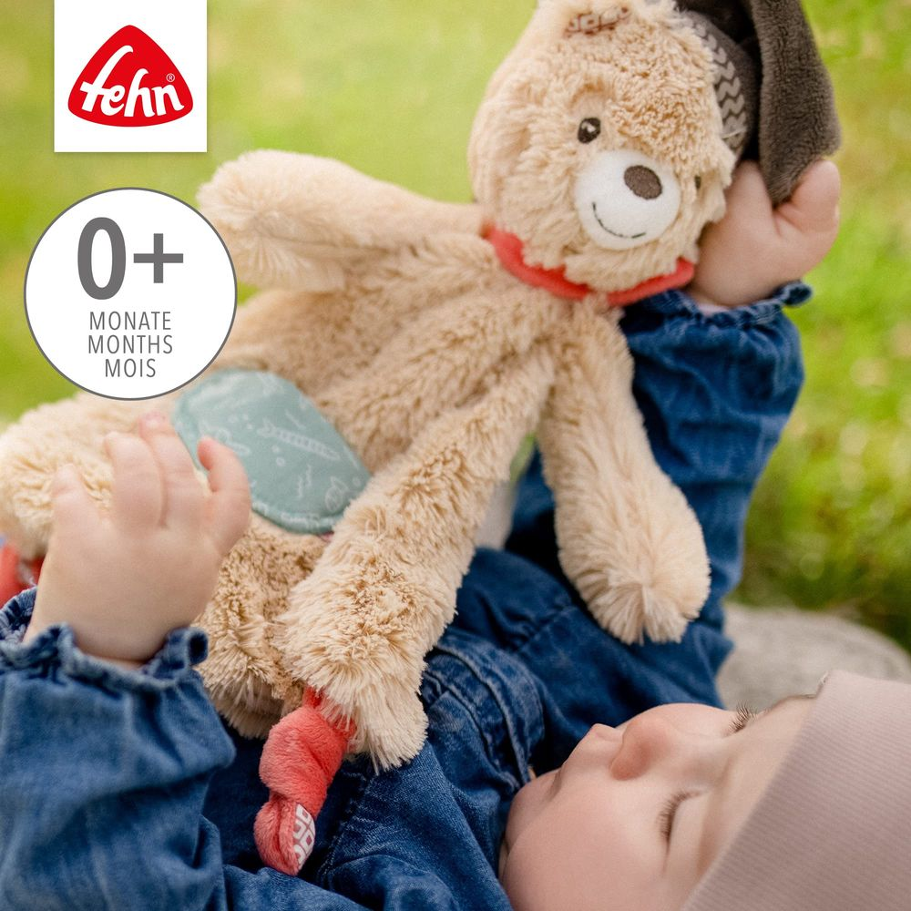 Ein Baby liegt mit einem braunen Kuscheltier im Gras.