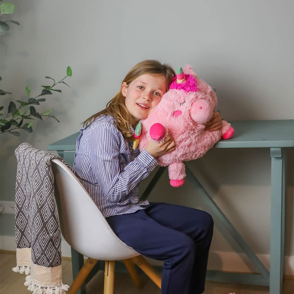 Ein Mädchen sitzt auf einem Stuhl und hält ein rosa Plüschtier, das wie ein Einhorn aussieht.