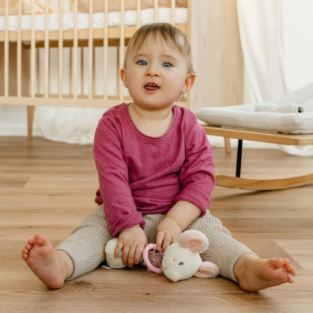 Un bambino siede sul pavimento di legno giocando con un peluche e un sonaglio.