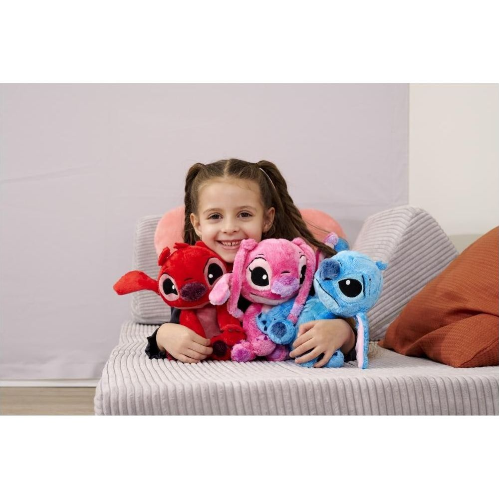 Dziewczynka trzyma na kanapie trzy pluszowe zabawki Stitch: czerwoną, różową i niebieską.
