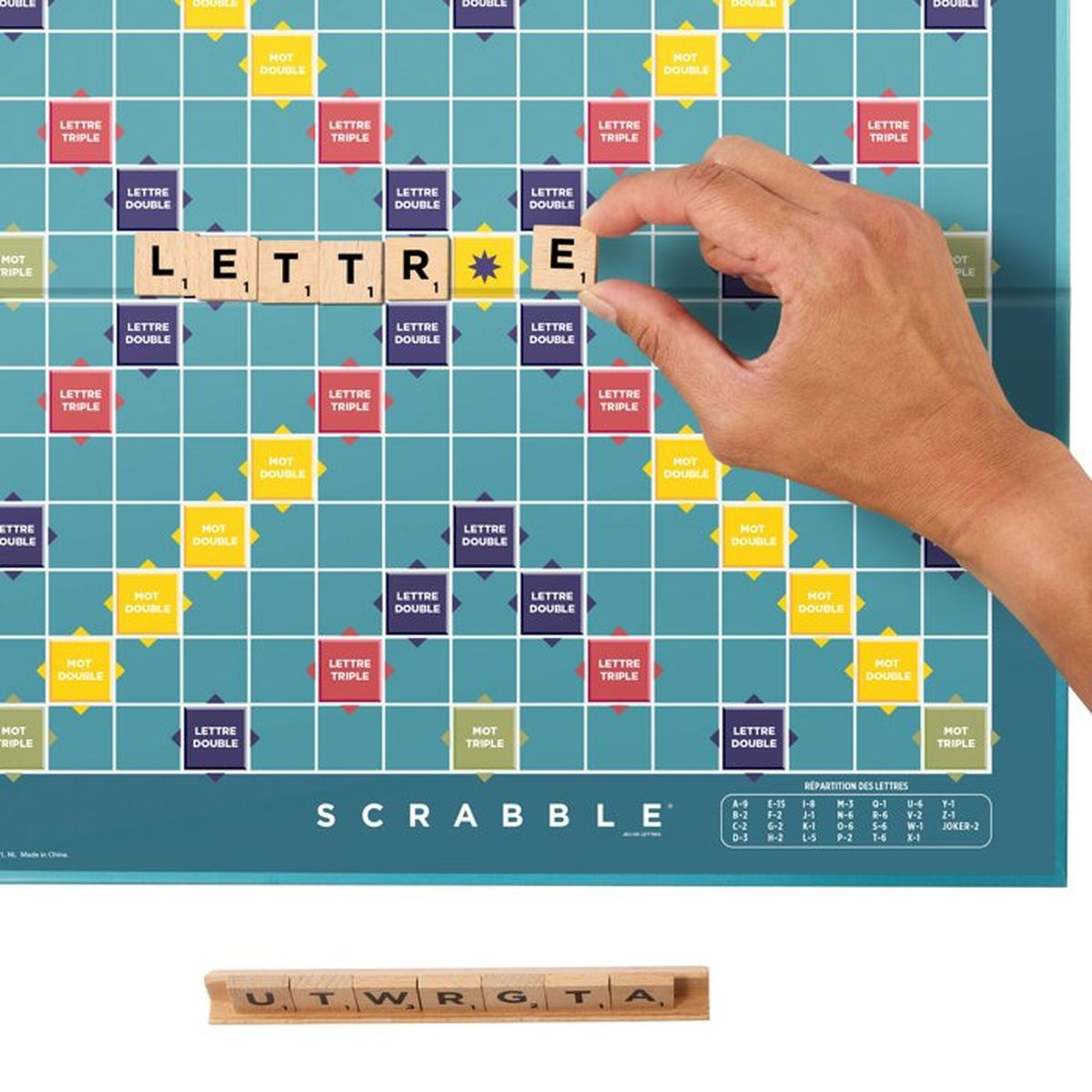 Ręka kładzie kafelki z literami 'LETTR E' na planszy Scrabble.