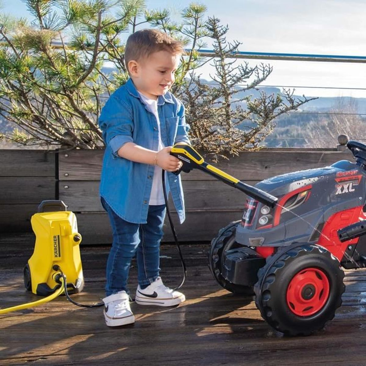 Un bambino con idropulitrice pulisce un trattore giocattolo.