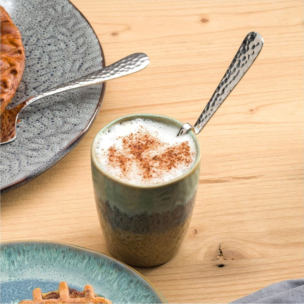 Tazza di caffè con schiuma e cannella, cucchiaio e pasticcini sui piatti.