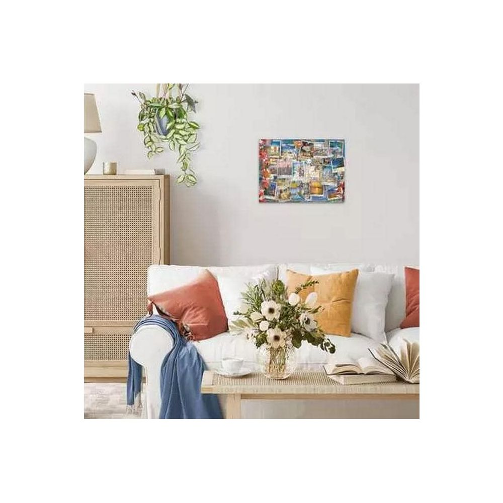 Un collage de photos de voyage est suspendu au-dessus d'un canapé blanc avec des coussins et un vase de fleurs.