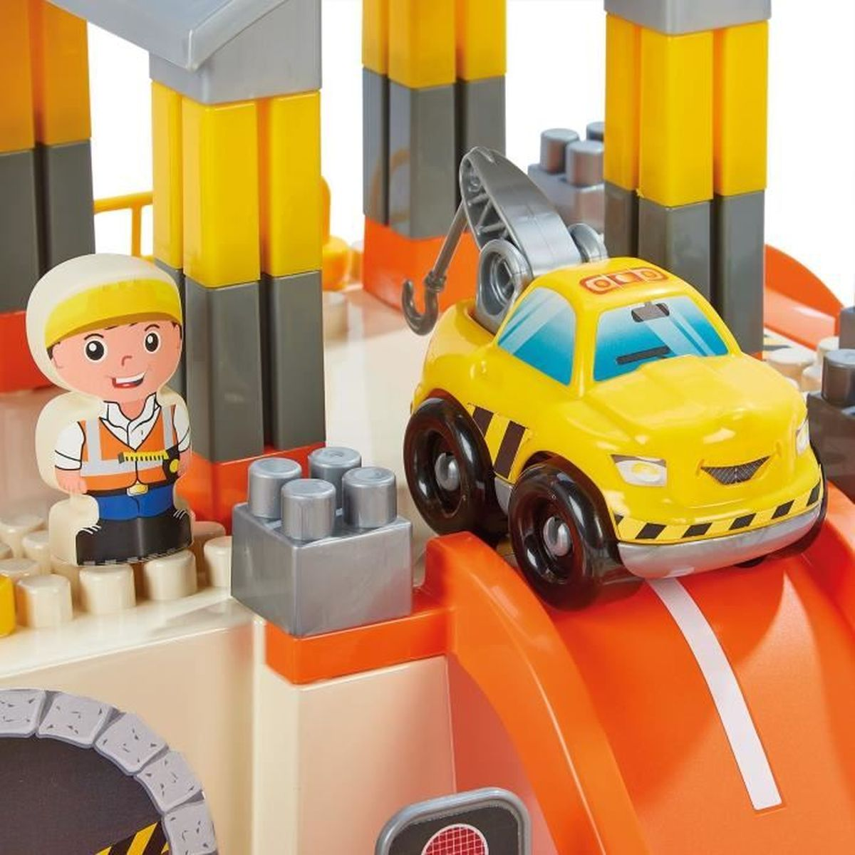 Gelber Spielzeug-Abschleppwagen mit Kran neben einem Bauarbeiter vor bunten Bausteinen.