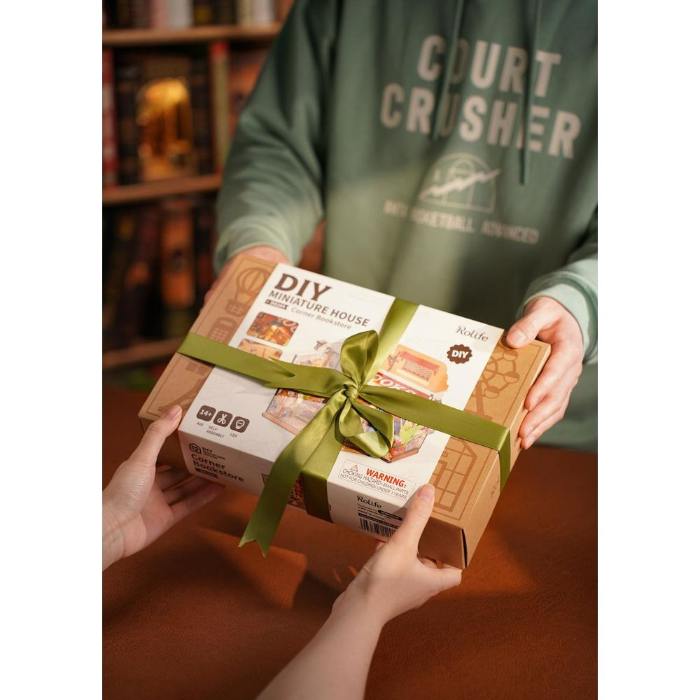 Dłonie wymieniają zapakowany domowy domek DIY, model „Corner Bookstore”.